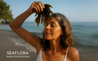 A woman in her 50s stands on a beach holding fresh seaweed in front of her face as golden seaweed oil gently drips onto her skin. Seaflora logo in white appears on the image.