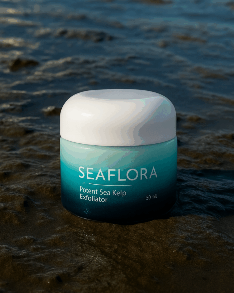 Potent Sea Kelp Facial Masque in Ocean Mud — Wild Seaweed Meets Mineral Skincare - Seaflora Skincare A Seaflora Potent Sea Kelp Exfoliator jar nestled in rich, dark ocean mud with fine mineral textures visible, highlighting its thalassotherapy roots. The turquoise ombré glass packaging contrasts naturally against the raw marine sediment, reinforcing its deep-cleansing, mineral-rich formulation.