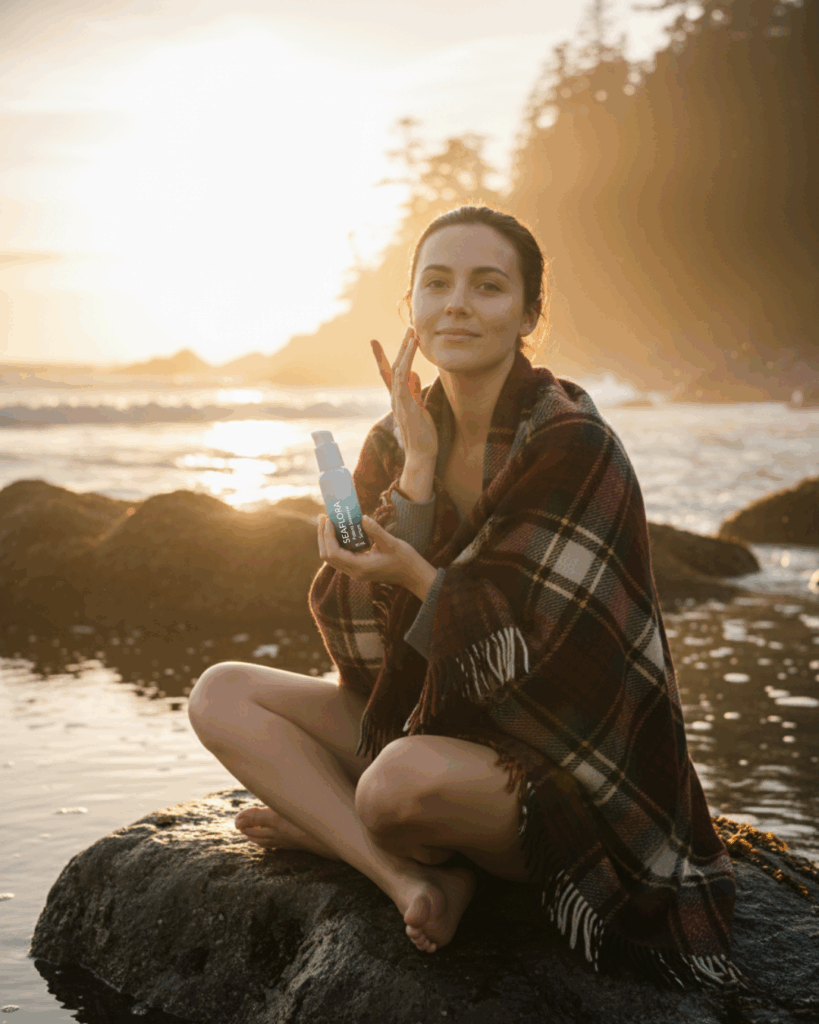 A lady applying Potent Seaweed Serum to her face on a rock by the ocean on the west coast of vancouver island in Autumn.