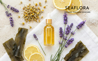 Flat lay of an amber dropper bottle surrounded by lemon slices, lavender sprigs, chamomile flowers, and dried seaweed strips on a marble background, with the Seaflora Organic Thalasso Skincare logo.